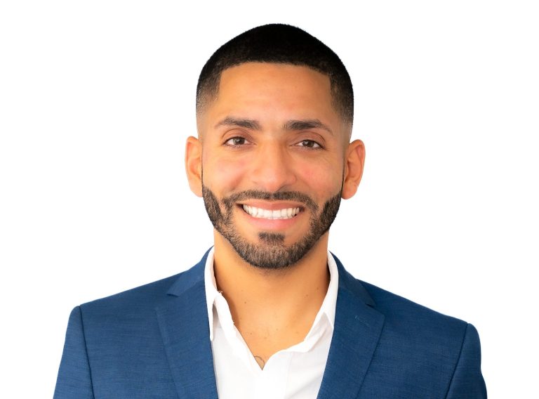 Man in a white shirt standing against a palm tree backdrop for a photo session.