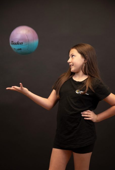 A girl in a black shirt poses with a floating volleyball in her hand at Miami photo studio