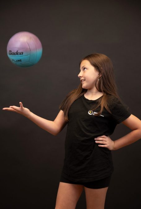 A girl in a black shirt poses with a floating volleyball in her hand at Miami photo studio