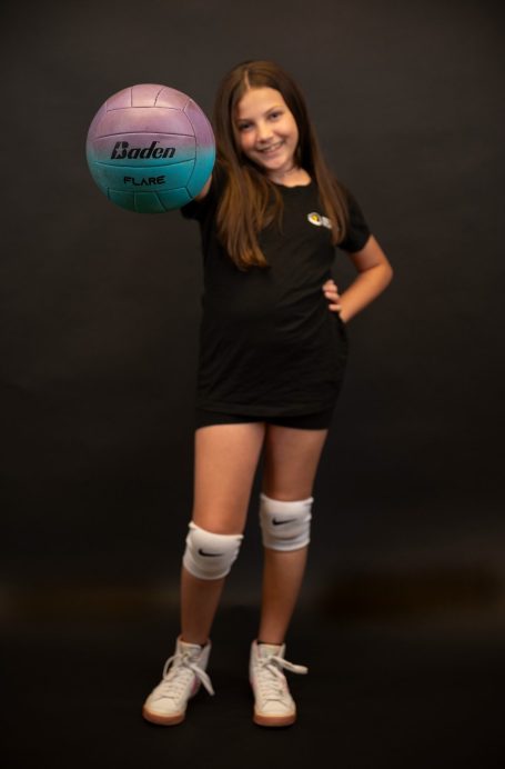 Volleyball athlete at Headshot Studio Portraits posing in a black shirt and white knee pads holding a colorful volleyball